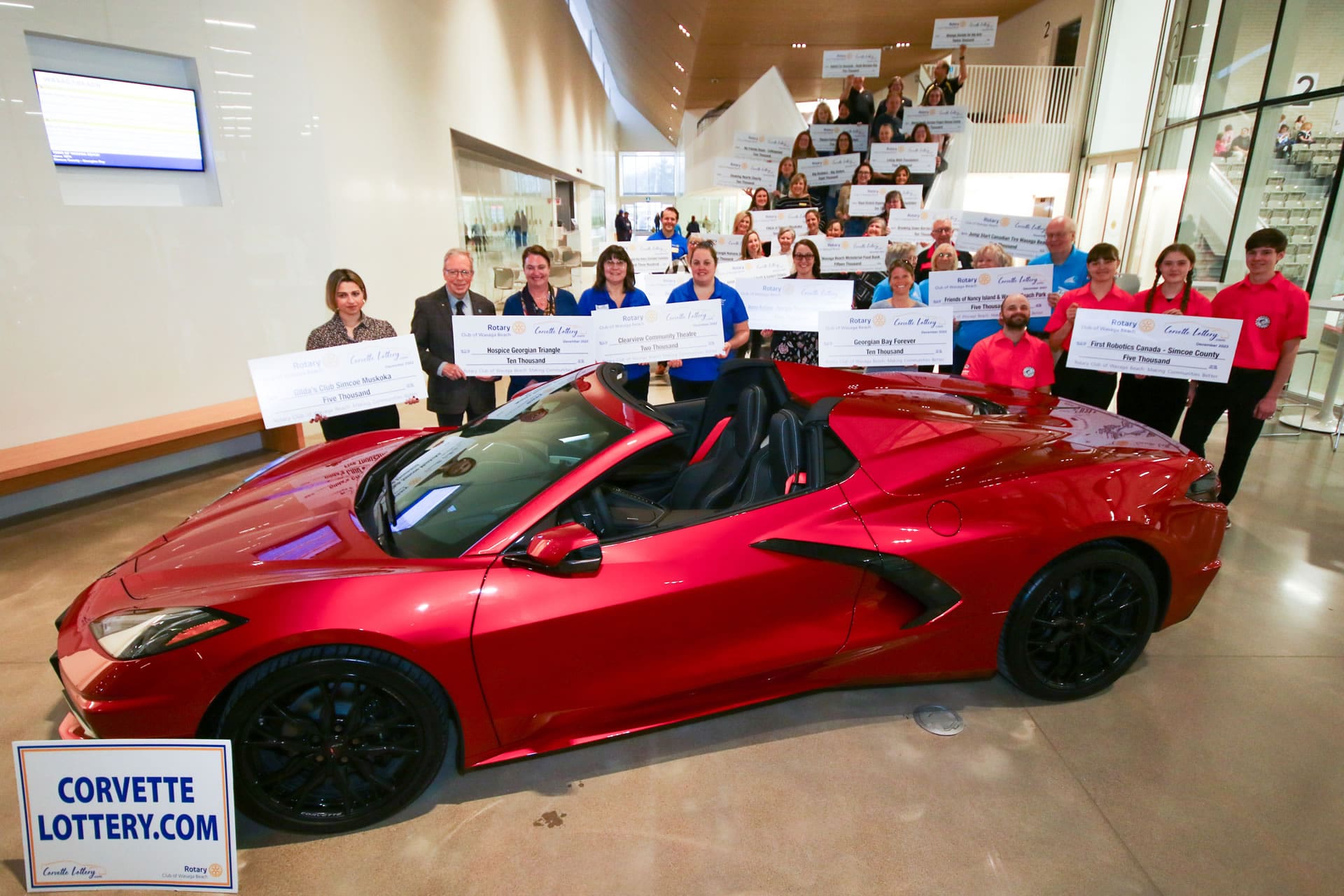Recipients of Corvette Lottery proceeds holding presentation cheques behind a Corvette Recipients of Corvette Lottery proceeds holding presentation cheques behind a Corvette